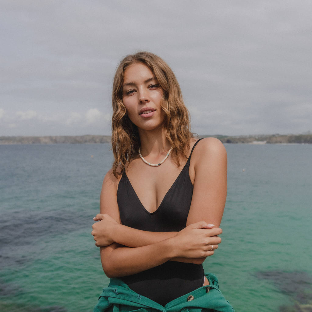 a woman in a black swimsuit standing by the water